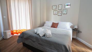 Een net opgemaakt bed met wit en bruin beddengoed, een nachtkastje met een lamp, en een muur met ingelijste foto's.