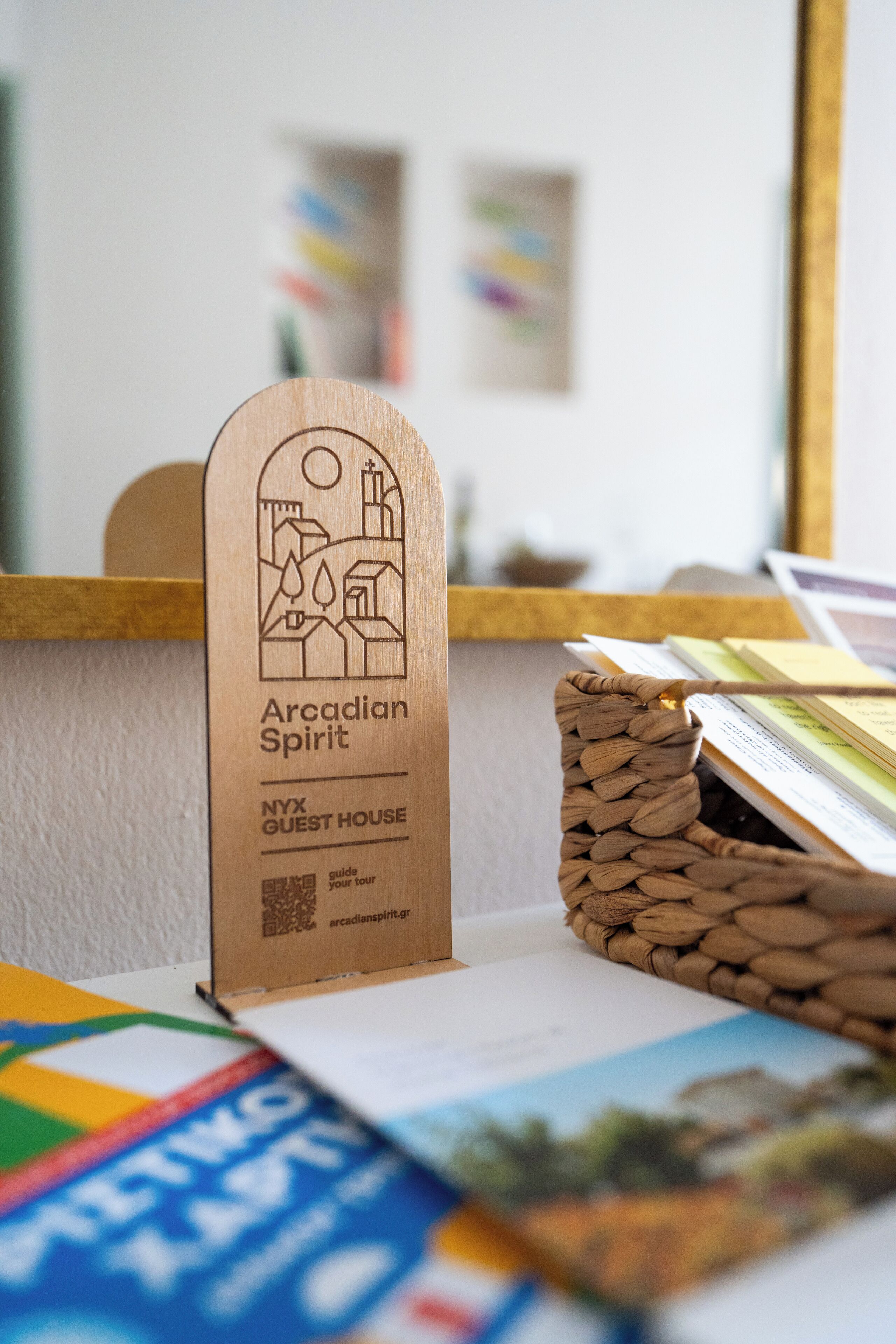 A wooden sign with the text "Arcadian Spirit" and "NYX GUEST HOUSE" along with a QR code.