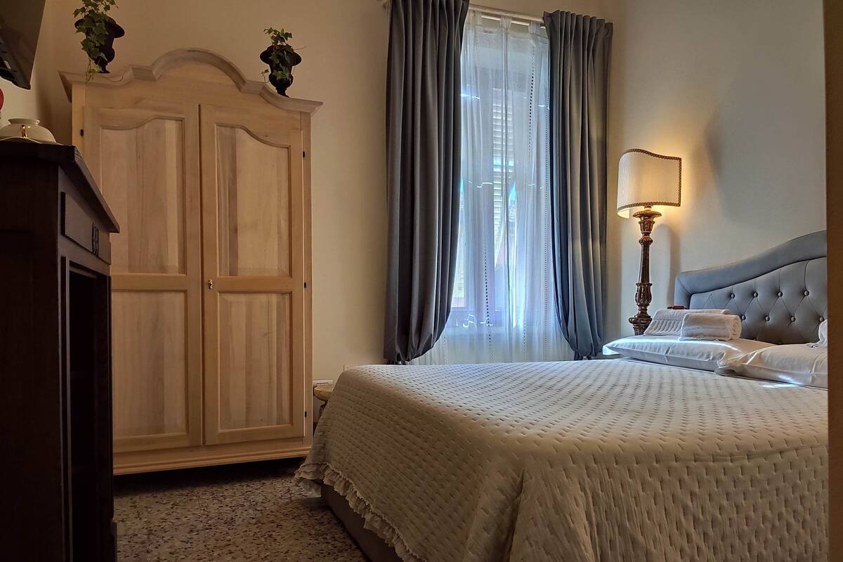 A bedroom with a large bed, a wardrobe, a window with curtains, and a bedside lamp.