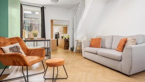 A modern living room with a sofa, armchair, and ottoman. A kitchen is visible in the background. - Free Parking | Near Aintree Racecourse & Anfield | Ideal for Contractors & Families (Liverpool)