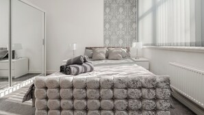 Un dormitorio moderno con una cama grande, una mesita de noche, una lámpara y una ventana con cortinas.