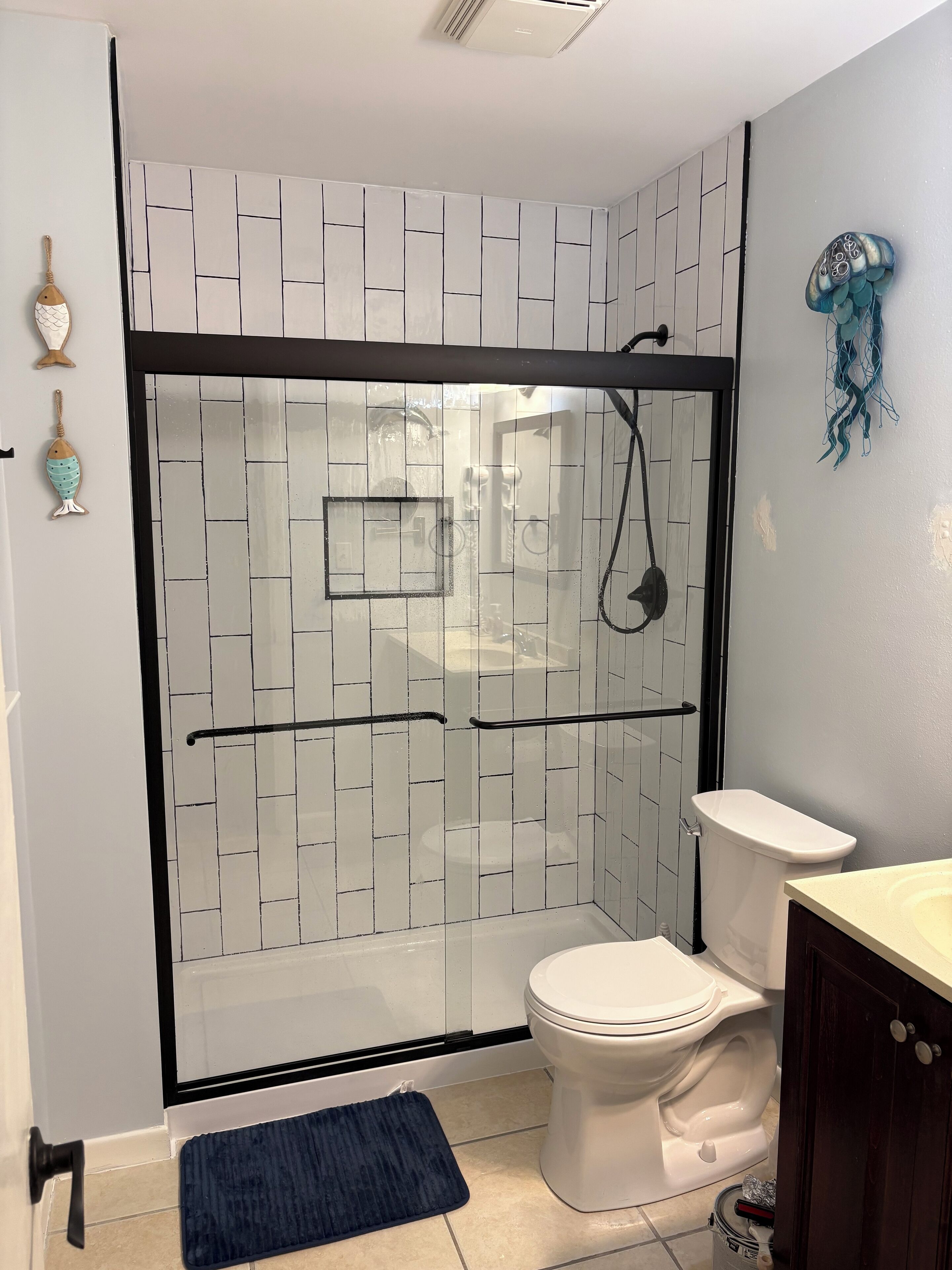 A bathroom with a glass shower enclosure, a toilet, a sink, and decorative fish ornaments.