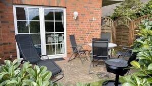 Eine Terrasse mit Grill, Liegestühlen und einem Tisch.