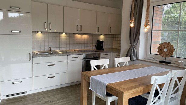 Eine moderne Küche mit weißen Schränken, einem Holztisch und einem Fenster mit Vorhängen.