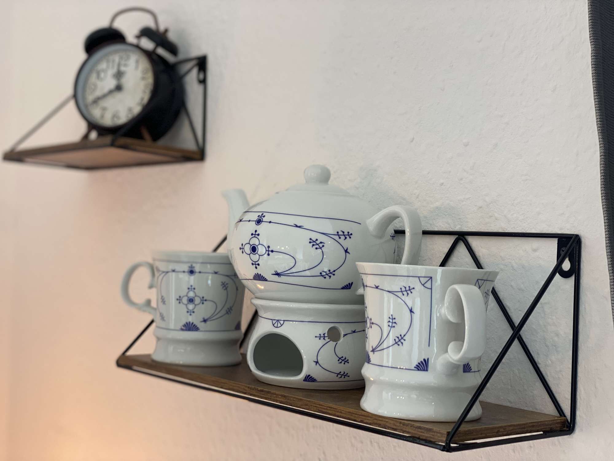 A wall-mounted shelf with a tea set and a clock.