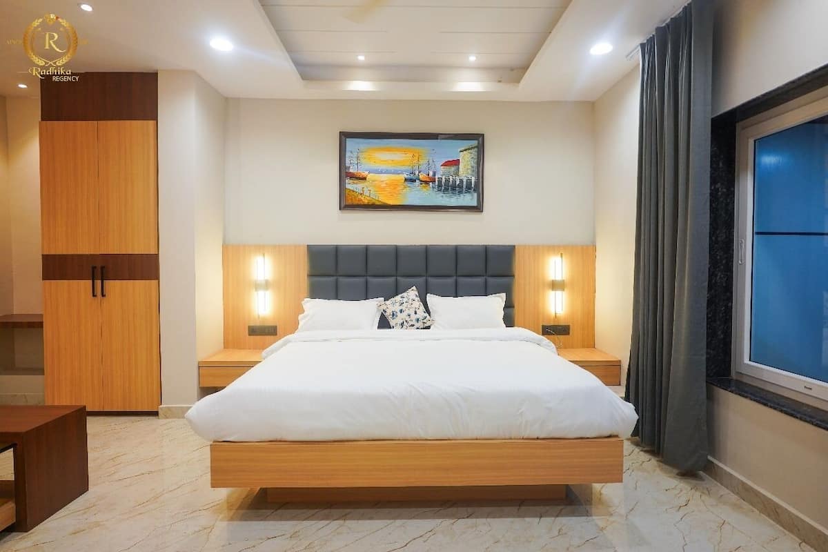 A modern bedroom with a large bed, wooden wardrobe, and a painting above the bed.