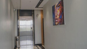 A hallway with a modern design, featuring a metallic elevator, a painting on the wall, and a patterned floor. - Hotel Radhika Regency (Balangir)