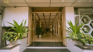 A modern hotel entrance with a glass door, a hallway leading inside, and potted plants on either side. - Hotel Radhika Regency (Balangir)