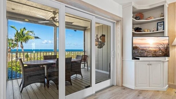 Un balcón con vista al océano, una mesa de comedor con sillas y un televisor sobre un mueble.
