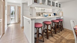 Una cocina moderna con armarios blancos, una isla central con taburetes de bar y vistas al exterior.
