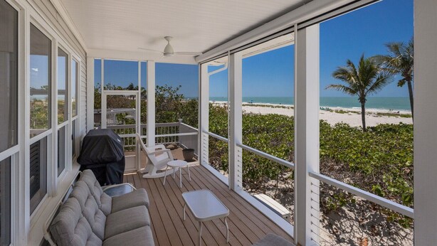 A covered outdoor area with a wooden deck, white furniture, and a view of the beach. - 390 Gulf - Beachfront, 4 bed - 4 bath Private Pool - Dog Friendly! (Boca Grande)