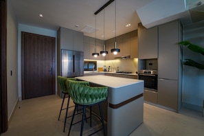 Una cocina moderna con una isla central, taburetes de bar, electrodomésticos de acero inoxidable e iluminación colgante.