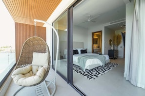 Quarto moderno com cama, cadeira suspensa e vista para a varanda.
