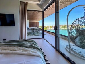 Une chambre d’hôtel moderne dotée d’un grand lit, d’une télévision et d’un balcon avec un fauteuil suspendu et une vue sur la mer.