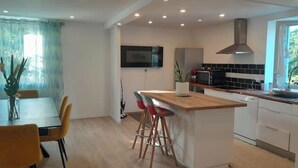 A modern kitchen with a central island, bar stools, a dining table with chairs, a microwave, and a TV mounted on the wall. - Stay in béarnais country (Baigts-de-Béarn)