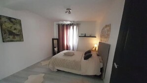 A bedroom with a bed, a nightstand, a wall-mounted shelf, a window with curtains, and a painting on the wall. - Stay in béarnais country (Baigts-de-Béarn)