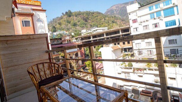 Un balcon avec une table en verre et des chaises en osier, d’où l’on peut admirer un paysage urbain avec des bâtiments et une montagne en arrière-plan.