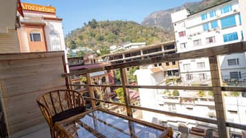 A balcony with a glass table and wicker chairs, overlooking a cityscape with buildings and a mountain in the background.