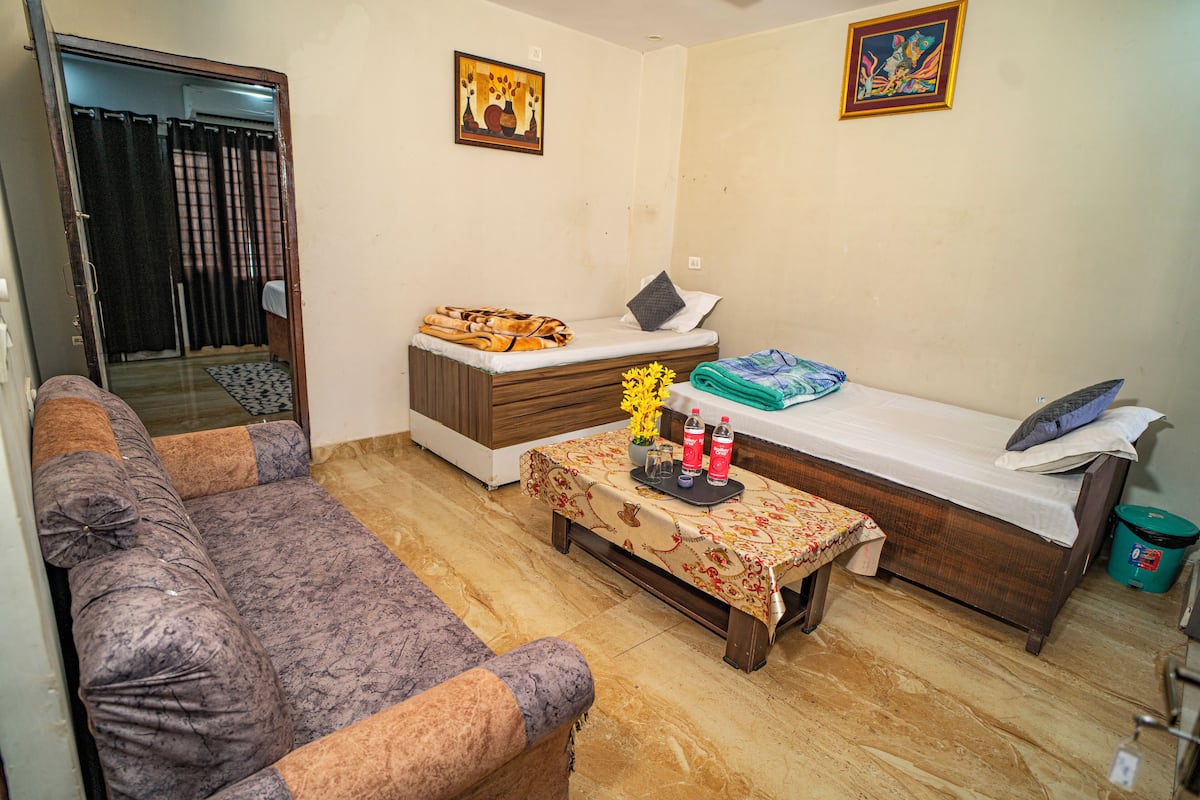 A compact living space with a sofa, a small table with decorative items, a bed, and two paintings on the walls.