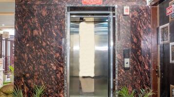 An elevator entrance with a marble wall, a sign above it, and two potted plants on either side.