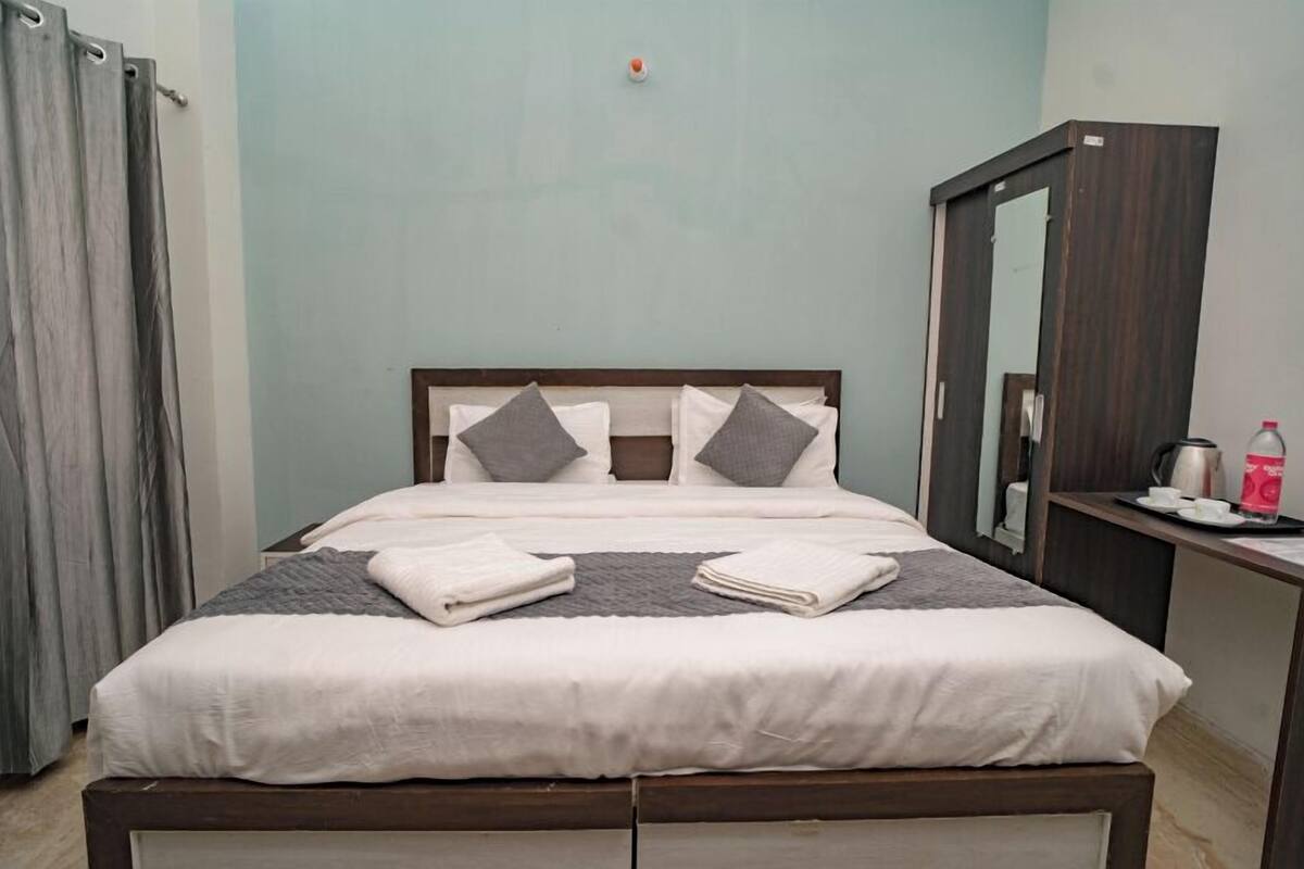 A neatly made bed with pillows, a bedside table with a cup and a bottle, and a mirror on the wall.