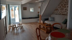 A spacious living area with a wooden floor, a sofa, a dining table with chairs, a staircase, and a view of the outside. - Maison la Tourterelle in Auvergne (Champs)