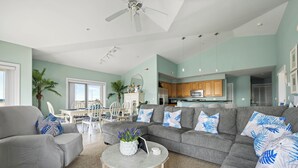 Ein geräumiges Wohnzimmer mit einem grauen Sofa, einem runden Couchtisch und einem Essbereich mit weißem Tisch und Stühlen.