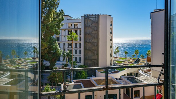 A high-rise building with a view of the ocean, featuring balconies and palm trees.