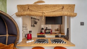 A compact kitchen with a TV, a red coffee maker, and a microwave. There are two stools and a small table with a bottle and a glass.
