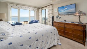 Un dormitorio con cama, cómoda, televisor y vista al océano.