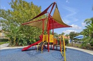 Un parque infantil con tobogán, estructuras de escalada y una zona sombreada.