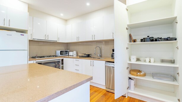A modern kitchen with white cabinets, a granite countertop, a microwave, a stove, and a dishwasher. - Stylish, modern and secure family home! (Heidelberg West)