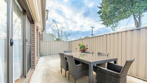 An outdoor patio with a glass door, a beige fence, and a table with wicker chairs. - Stylish, modern and secure family home! (Heidelberg West)