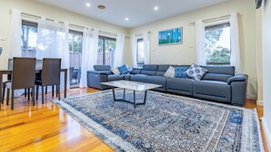 A spacious living room with a grey sofa, a coffee table, and a patterned rug. - Stylish, modern and secure family home! (Heidelberg West)