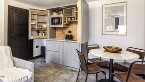 A compact kitchen with built-in shelves, a coffee machine, and a dining area with a round table and chairs.
