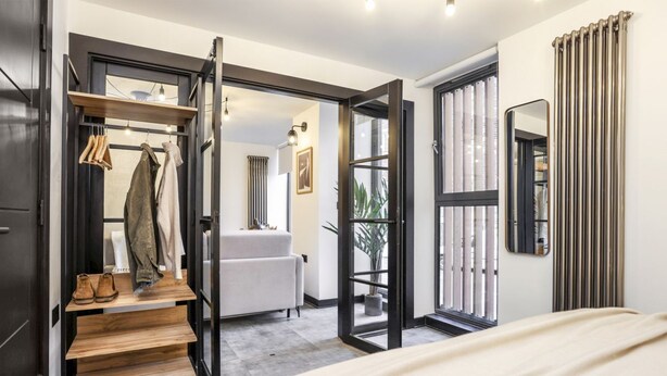 A modern bedroom with a bed, a wooden shoe rack, a white sofa, and a large window.