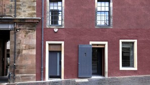 A red building with a stone facade, a closed dark blue door, and a window with a sign above it.