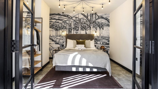 A bedroom with a large bed, a modern chandelier, and a wall mural.