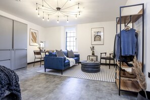 Un salon moderne avec un canapé bleu, une table basse ronde et un portant à vêtements.