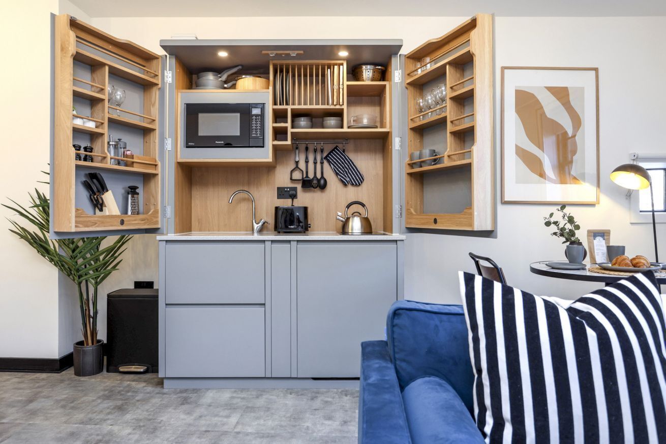 A compact kitchen with built-in appliances, wooden shelves, and a blue sofa with striped pillows.