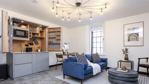 Un soggiorno moderno con un divano blu, un tavolino rotondo e una zona cucina con elettrodomestici integrati e scaffalature.
