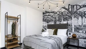A modern bedroom with a bed, a wooden shelf, a nightstand, and a large black and white mural on the wall. - Laboratory Store: 2bed moments from Royal Mile (Edinburgh)