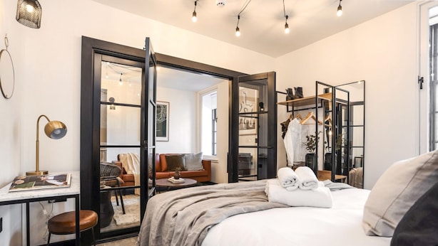 Ein modernes Hotelzimmer mit einem großen Bett, einem Schreibtisch mit Lampe, einem Kleiderschrank und einer Sitzecke mit Sofa und Sessel.