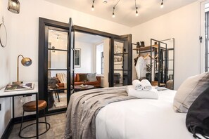 Une chambre d’hôtel moderne dotée d’un grand lit, d’un bureau avec une lampe, d’une armoire et d’un coin salon avec un canapé et un fauteuil.