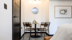 A small, modern room with a round table and two chairs, a mirror on the wall, and a framed picture.