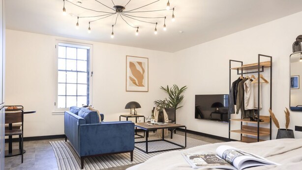 A modern bedroom with a large bed, a blue sofa, a dining table, and a TV. - Engineering: Deluxe Studio w/City Views-2nd floor (Edinburgh)