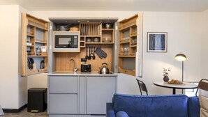 A compact kitchen with built-in appliances, wooden shelves, and a blue sofa in a modern living area. - Engineering: Deluxe Studio w/City Views-2nd floor (Edinburgh)