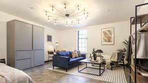 A modern living room with a blue sofa, a coffee table, a large wardrobe, and a chandelier. - Engineering: Deluxe Studio w/City Views-2nd floor (Edinburgh)