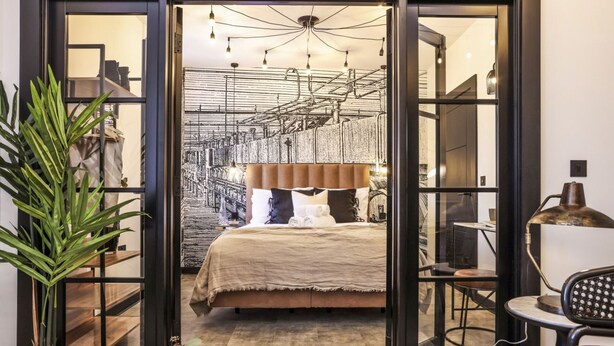A modern bedroom with a large bed, a desk, and a chair. There is a plant on the left side and a lamp on the right side. - Locker Room:  Stylish 2bed w/City Views-3rd floor (Edinburgh)
