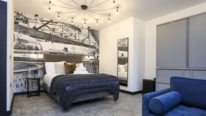 Un dormitorio con una cama grande, un sofá azul, un mural en la pared y una lámpara de techo moderna.